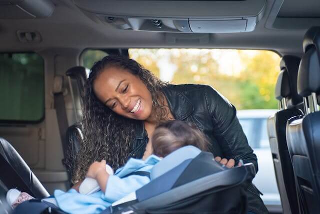 woman looking at infant in car seat