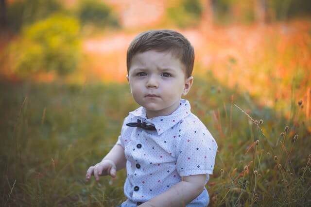 young toddler boy standing in the grass in a button-up white shirt and black bowtie.