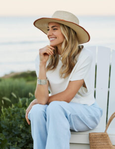 Woman sitting at the beachc wearing a ravello linen chambray stripe pant and white cap sleeve sweater