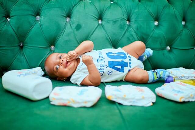 baby surrounded by baby items on a green velvet sofa