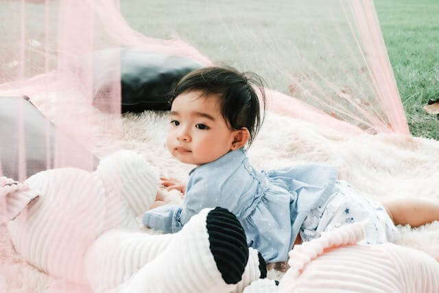 baby laying in netted sun play area in grass